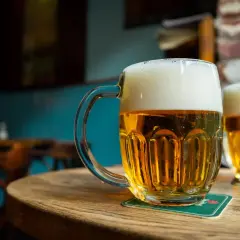 Dwa kufle złocistego piwa miodowego gryczanego z obfitą pianką stoją na drewnianym stole w przytulnym pubie.