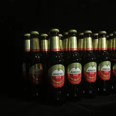 Rząd butelek piwa Amstel, kultowe piwo, w ciemnym otoczeniu.