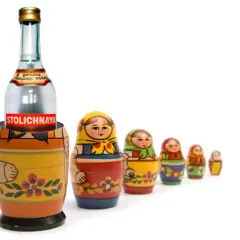 Butelka wódki Stolichnaya w drewnianej babuszce, otoczona mniejszymi matrioszkami.