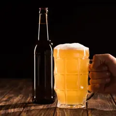 Ręka trzymająca kufel ze złotym piwem, obok butelka. Idealne na wieczór z piwem wędzonym.