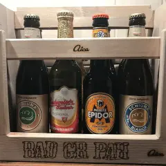 Drewniana skrzynka z piwami. Na pierwszym planie piwo w zielonej puszce, obok inne butelki. Na skrzynce napis "BAD CR PAH".