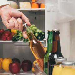 Ręka wyjmuje z lodówki butelkę piwa. Czy piwo może się zepsuć? W lodówce są też inne napoje i owoce.