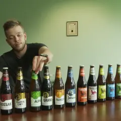 Mężczyzna wybiera piwo bez drożdży z rzędu butelek. Widać różne rodzaje piw, m.in. APA, Koźlak, Złote Lwy.