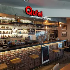 Wnętrze Qufel beer park z barem, butelkami piwa i menu.