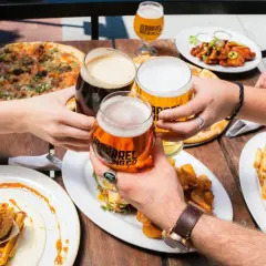 Ludzie wznoszą toasty piwem, celebrując spożycie piwa na świecie przy stole pełnym pizzy, burgerów i kurczaka z goframi.