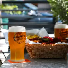 Orzeźwiające weizen piwo z pianką, obok koszyk z przekąskami i drugie piwo.
