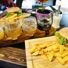 Degustacja piw z Browaru Rzeszowskiego: trzy kufle z jasnym i ciemnym piwem, obok burgery i frytki.
