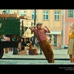 Mężczyzna w czapce i szelkach opiera się o ciężarówkę z piwem Žatecký. Ile procent ma to piwo? Kobieta w żółtej bluzce patrzy w górę.