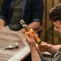 Mężczyzna trzyma butelkę piwa 8 procent, gotowy do otwarcia. Na stole leży otwieracz.