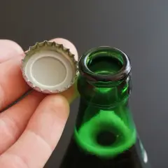 Dłoń trzymająca kapsel, obok zielona szyjka butelki. Czas na piwo! Jak otworzyć piwo?