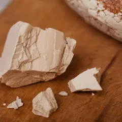 Kawałki świeżych drożdży na drewnianej desce. Obok leży bochenek chleba. Te przeterminowane drożdże już nie wyrosną.