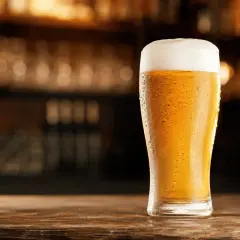 Chłodne pils piwo z obfitą pianką, skraplające się od orzeźwienia, stoi na drewnianym blacie.