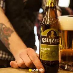 Ręka z tatuażem sięga po butelkę piwa Książęce Golden Ale. Czy to piwo jest gorzkie?