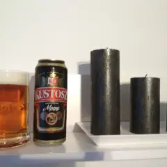Kufel piwa i puszka Kustosz Mocne obok trzech czarnych świec.