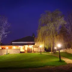Wieczorem oświetlony browar Wojkówka z kamiennymi murami i zielonym trawnikiem.