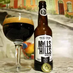Szklanka z ciemnym imperial stout i butelka piwa Mills and Hills na tle malarskiej sceny.