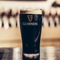 Szklanka ciemnego piwa stout Guinness z pianką na wierzchu, na drewnianym blacie.