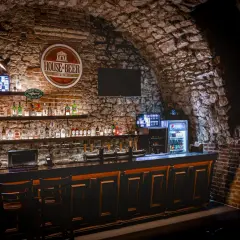 Wnętrze "House of Beer" z kamiennymi ścianami, barem pełnym butelek i kranów piwnych.
