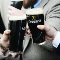 Dwie osoby wznoszą toast szklankami ciemnego piwa Guinness. Zastanawiasz się, ile procent alkoholu ma Guinness?