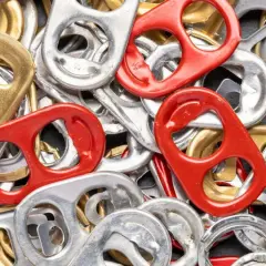 Mnóstwo srebrnych, złotych i czerwonych zawleczek od puszek tworzy barwną mozaikę. Co oznaczają zawleczki od puszek? To symbol recyklingu i możliwości tworzenia z nich czegoś nowego.
