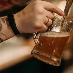 Ręka z tatuażami nalewa złociste piwo z nalewaka do szklanki.