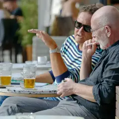 Dwóch mężczyzn przy stoliku, jeden pali, drugi gestykuluje. Przed nimi piwo. Idealny wieczór, może nawet piwo przed snem.