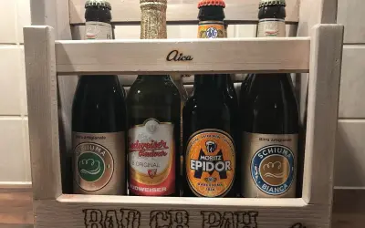 Drewniana skrzynka z piwami. Na pierwszym planie piwo w zielonej puszce, obok inne butelki. Na skrzynce napis "BAD CR PAH".