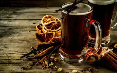 Dwa kufle ciemnego piwa korzennego, ozdobione laskami wanilii, na tle suszonych pomarańczy i przypraw.