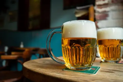 Dwa kufle złocistego piwa miodowego gryczanego z obfitą pianką stoją na drewnianym stole w przytulnym pubie.
