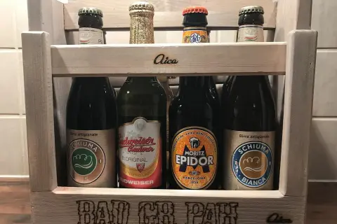 Drewniana skrzynka z piwami. Na pierwszym planie piwo w zielonej puszce, obok inne butelki. Na skrzynce napis "BAD CR PAH".