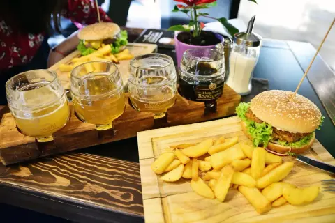 Degustacja piw z Browaru Rzeszowskiego: trzy kufle z jasnym i ciemnym piwem, obok burgery i frytki.