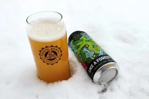Szklanka piwa z logo "Trzech Kumpli" i puszka "Like a Forest" od **browaru Nepomucen** w śniegu.