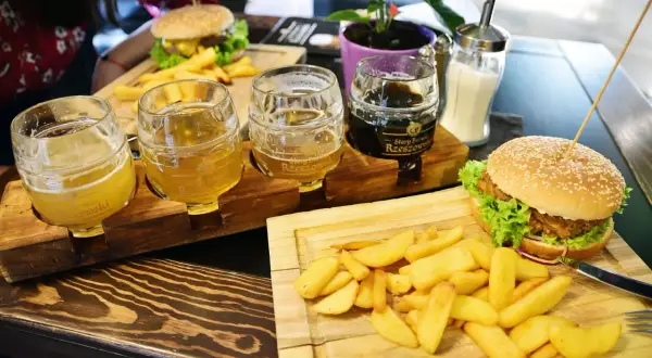 Degustacja piw z Browaru Rzeszowskiego: trzy kufle z jasnym i ciemnym piwem, obok burgery i frytki.