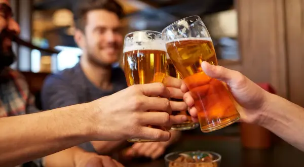Trzech przyjaciół wznosi toast piwem, zastanawiając się, czy piwo to alkohol.