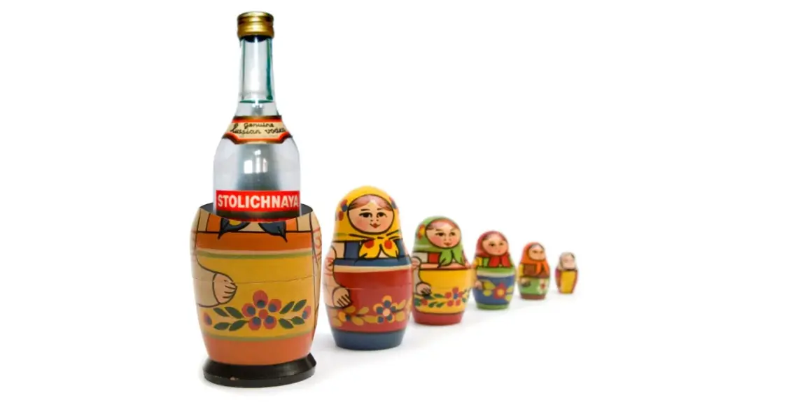 Butelka wódki Stolichnaya w drewnianej babuszce, otoczona mniejszymi matrioszkami.