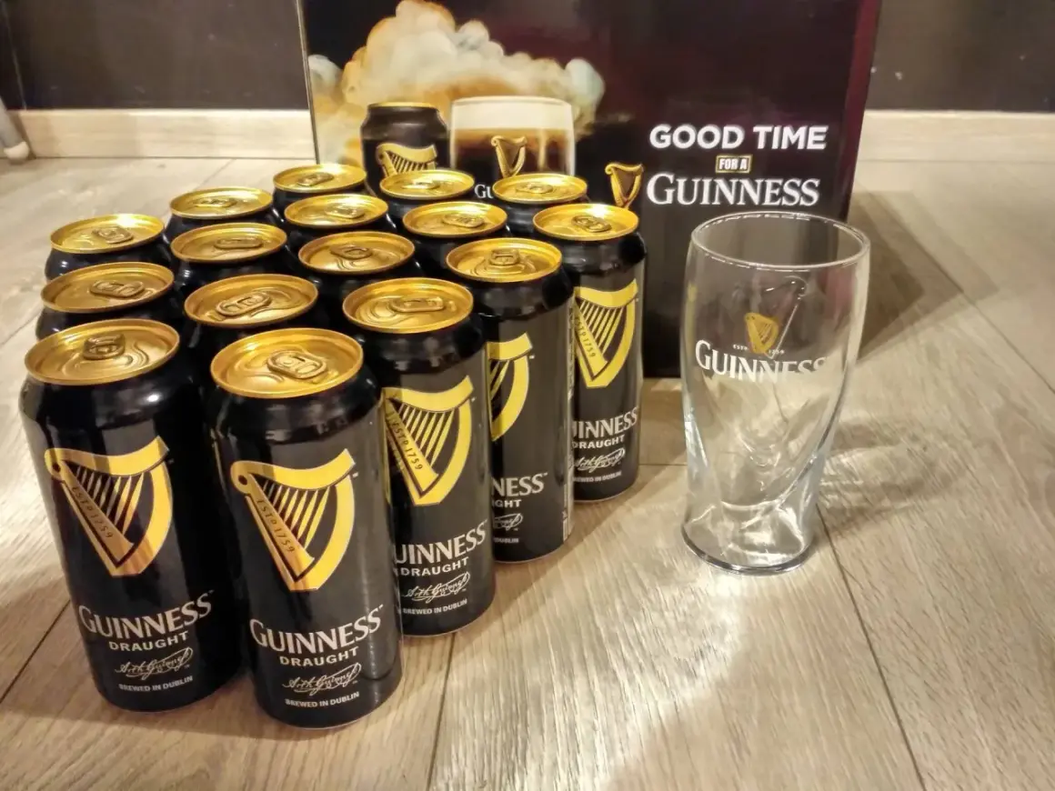 Dużo puszek Guinness z złotymi wieczkami i pustą szklanką, gotowe na dobrą zabawę z Guinness.