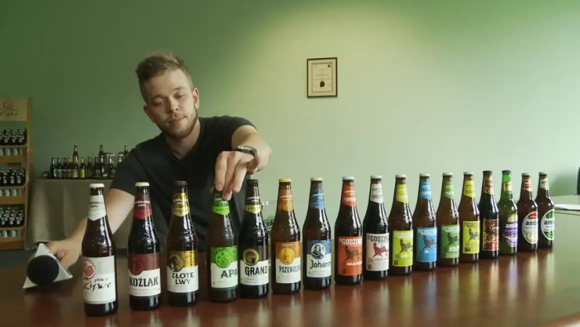 Mężczyzna wybiera piwo bez drożdży z rzędu butelek. Widać różne rodzaje piw, m.in. APA, Koźlak, Złote Lwy.