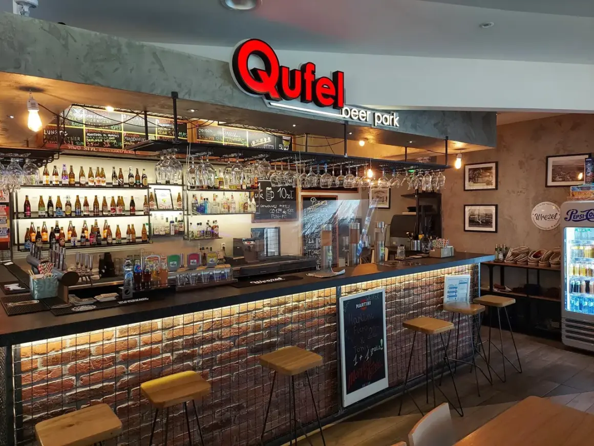 Wnętrze Qufel beer park z barem, butelkami piwa i menu.
