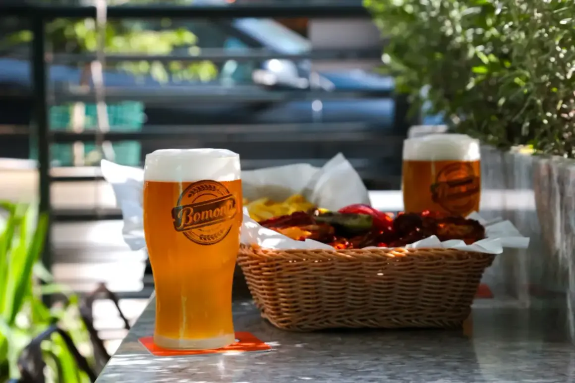 Orzeźwiające weizen piwo z pianką, obok koszyk z przekąskami i drugie piwo.