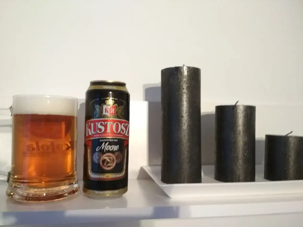 Kufel piwa i puszka Kustosz Mocne obok trzech czarnych świec.