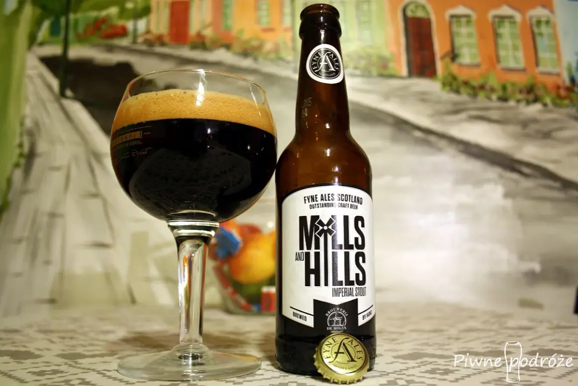 Szklanka z ciemnym imperial stout i butelka piwa Mills and Hills na tle malarskiej sceny.