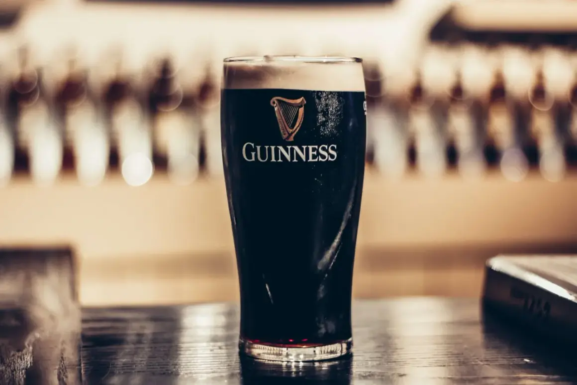 Szklanka ciemnego piwa stout Guinness z pianką na wierzchu, na drewnianym blacie.