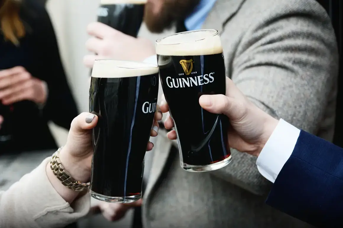 Dwie osoby wznoszą toast szklankami ciemnego piwa Guinness. Zastanawiasz się, ile procent alkoholu ma Guinness?