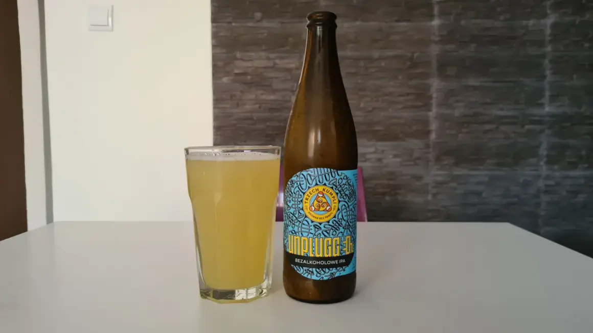 Bączek piwa "Unplugged" bezalkoholowe IPA i szklanka orzeźwiającego napoju na białym stole.