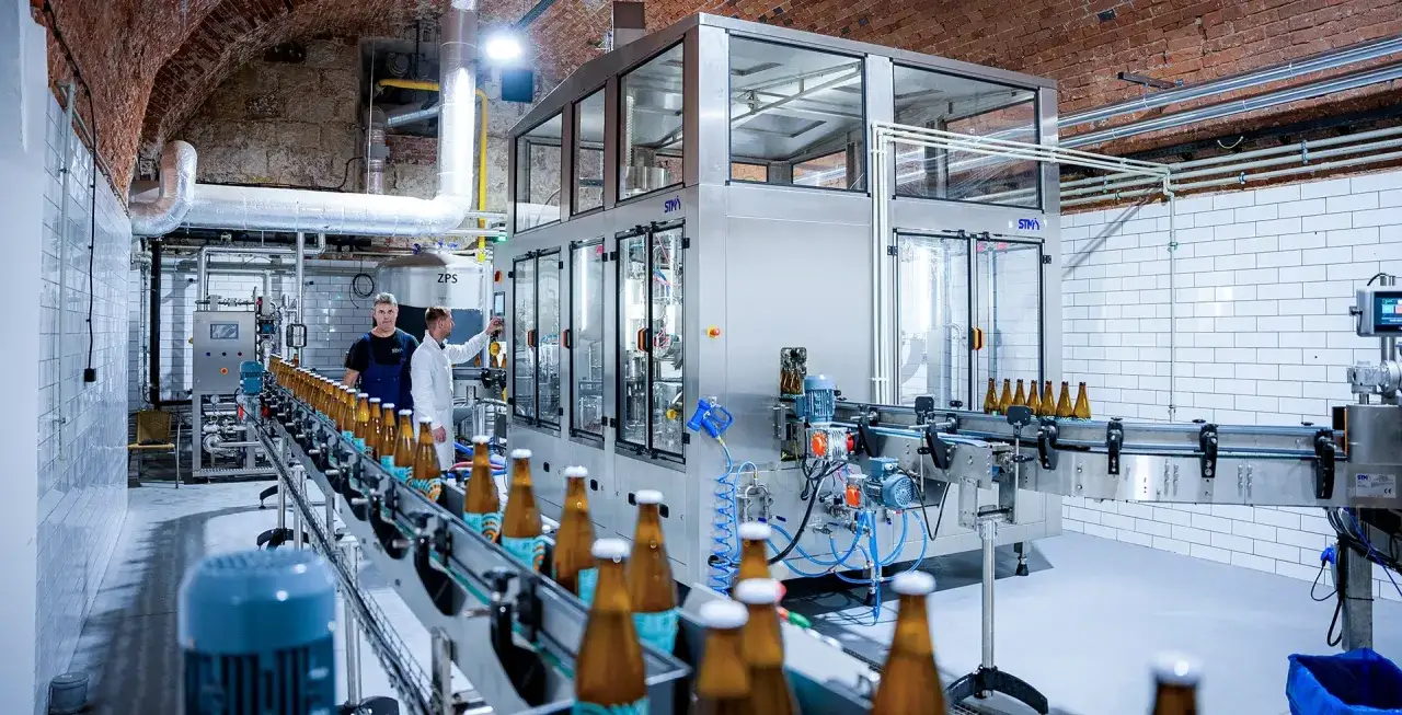 Nowoczesne automaty do butelek pracują w browarze. Pracownicy nadzorują linię produkcyjną z butelkami piwa.
