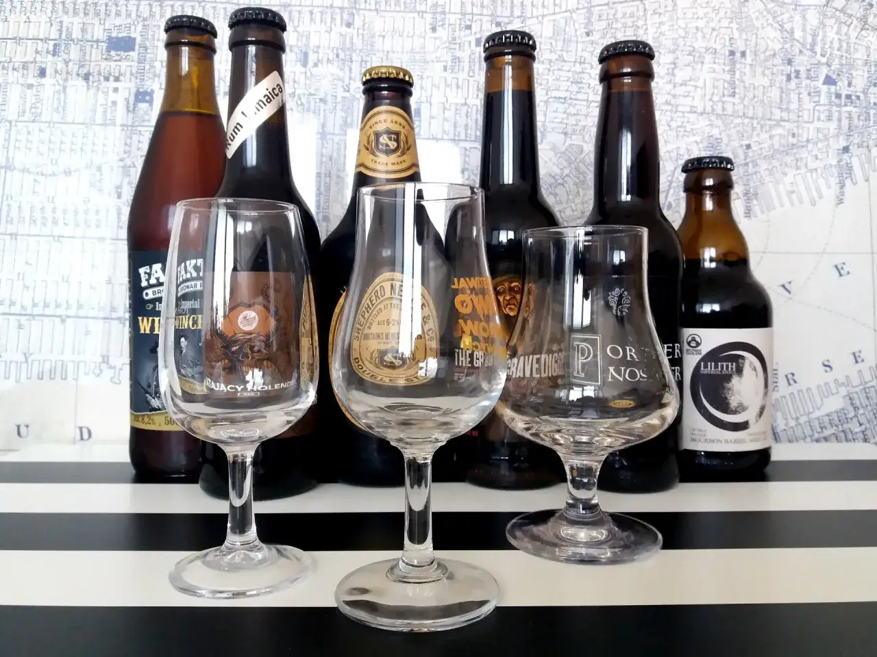 Butelki z piwem i kieliszki do degustacji. W tle mapa, a na stole pasy. Wspaniały wybór, ale alkohol.
