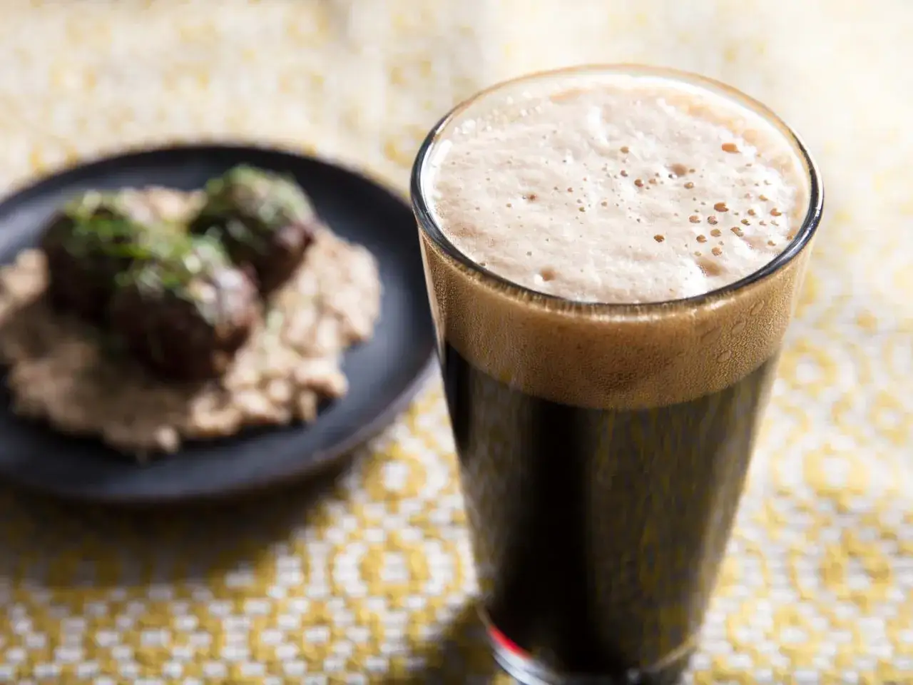 Gęsta piana na ciemnym piwie stout, obok talerz z klopsikami na puree. Idealne połączenie smak&oacute;w.