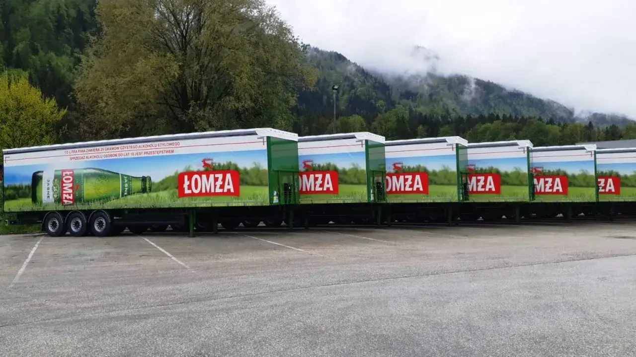 Rząd naczep z reklamą piwa Łomża, gotowych do transportu.