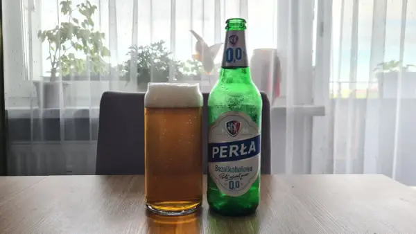 Szklanka i butelka Perły Bezalkoholowej. Perła wśród piw, 0,0% alkoholu, idealna na orzeźwienie.