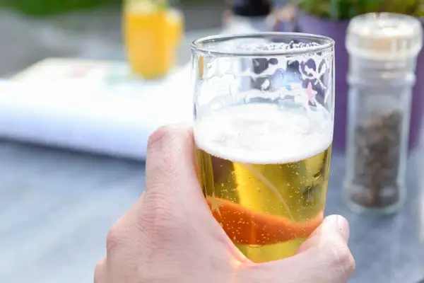 Dłoń trzymająca szklankę złotego piwa z pianką. Idealne piwo dla kobiet na letni wieczór.